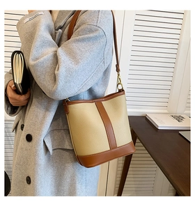 Detail of a vintage beige bucket bag with brown leather trim worn with a grey wool coat