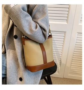 Detail of contrast-colored bucket bag in beige and brown lychee grain leather with gold hardware
