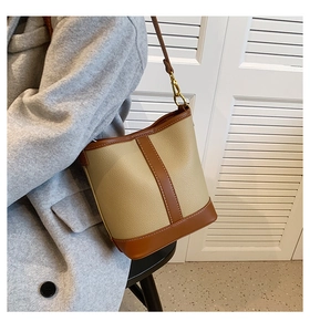 Beige bucket bag with brown trim shown styled on a grey coat with white background