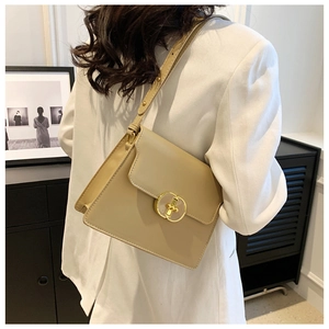 Détail d'un sac bandoulière en cuir beige avec fermoir doré sur une veste blanche