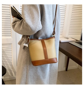 Detail of a contrast leather bucket bag worn with a grey coat in a home office setting