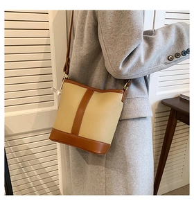 Close-up of contrast stitching on beige and brown leather bucket bag worn by model