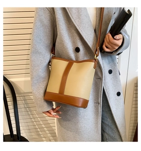 Detail of a chic color-block bucket bag with beige leather and brown trim on a model