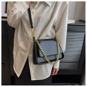 Detailed view of black crossbody bag with gold chain strap on white shirt outfit