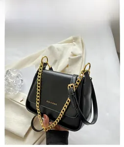 Detail of matte black leather crossbody bag with gold chain strap and metal logo