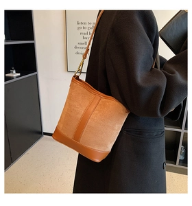 Detail of tan patchwork bucket bag featuring suede and smooth leather with gold metal buckle
