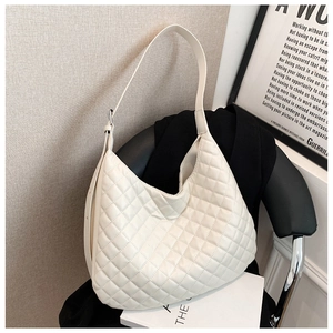 Detail of cream quilted tote bag with hobo silhouette on modern chair background