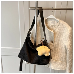 Detailed texture of black suede shoulder bag with gold hardware and yellow plush pendant