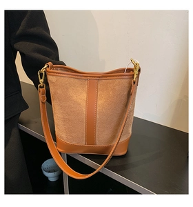 Detail of a brown suede bucket bag with smooth leather stitching and golden metal hook