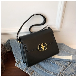 Gros plan du sac bandoulière en cuir mat noir avec boucle dorée sur veste en jean