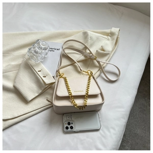 Detail of a creamy white crossbody bag with thick gold chain on a beige blazer background