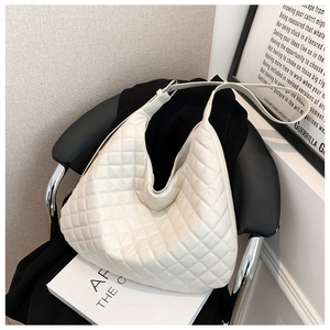Detail of white quilted hobo bag with adjustable silver buckle on a minimalist chair