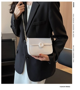Close-up of a white leather crossbody bag with gold chain and circular buckle detail