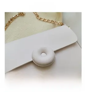 Detail of white PU leather crossbody bag featuring unique round buckle and gold chain strap