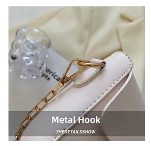 Close-up of golden metal hooks and chain details on a cream-colored leather handbag