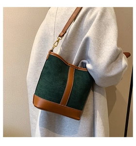 Detail of dark green suede bucket bag with brown leather trim and white contrast stitching
