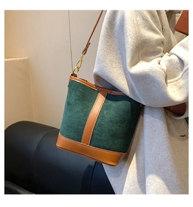 Detail of a retro bucket bag featuring green suede and brown leather trim on a model