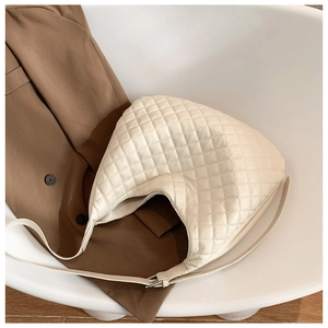 Close-up of cream quilted crescent bag with adjustable strap on a brown coat background