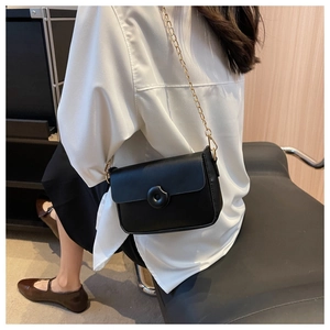 Detailed view of black leather crossbody bag featuring gold chain strap and round buckle