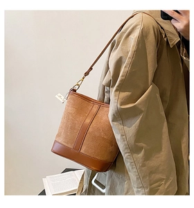 Detail of a brown suede bucket bag with leather accents and gold hardware on a model