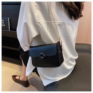 Detail of a black crossbody square bag featuring a gold chain and circular metal buckle
