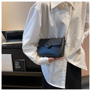Close-up of black leather crossbody bag with round buckle and golden chain strap