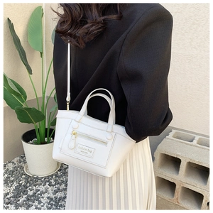 Détail d'un sac bandoulière blanc avec étiquette mode et zip doré porté par un mannequin