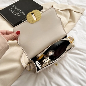 Sac bandoulière chic en cuir crème avec boucle dorée et essentiels posés sur un lit