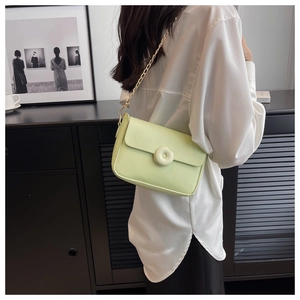 Close-up of a cream green crossbody bag with a round buckle and gold chain strap