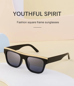 Detail of square black sunglasses with gold metal top trim and dark grey lenses