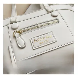 Détail du sac blanc montrant la fermeture dorée et l'écusson de la marque en gros plan
