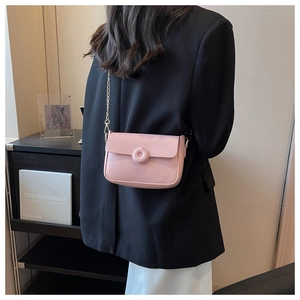 Detail showing a light pink crossbody square bag with unique circular donut buckle and gold chain