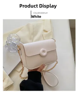 Detail of white mini crossbody bag with round buckle and gold chain strap on beige blazer