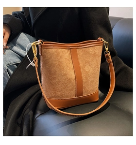 Detail of a brown suede bucket bag with leather trim on a black leather sofa