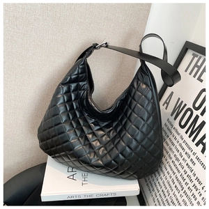 Detail of black quilted hobo shoulder bag with rhombus pattern on an art book