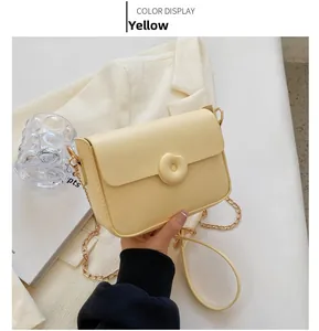 Detail of yellow crossbody bag with gold chain and circular clasp on white blazer