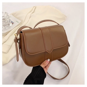 Nahaufnahme der karamellfarbenen Satteltasche mit goldener Schnalle auf hellem Stoff