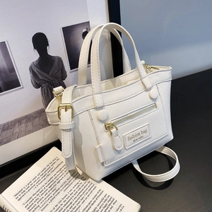 Sac à main minimaliste en cuir PU beige avec détails dorés et bandoulière sur un livre