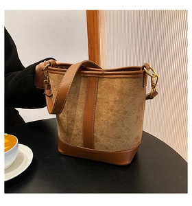 Close-up of brown suede and leather patchwork bucket bag with shiny gold metal hardware