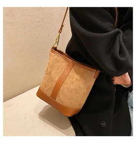 Detail of brown bucket bag showing suede and leather texture with gold hardware on a coat