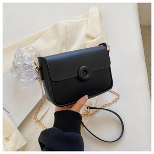 Detail of a black leather crossbody bag with round buckle and gold chain strap on blazer