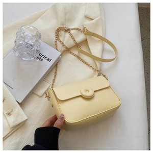 Detail of a creamy yellow crossbody bag with round decorative buckle and chain strap