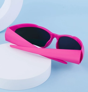 Detail der pinkfarbenen Y2K-Sportsonnenbrille auf weißem Ständer vor blauem Grund
