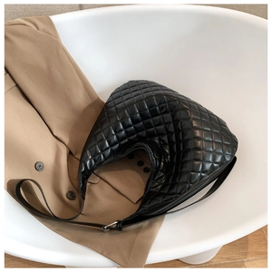 Close-up of black quilted leather hobo bag with adjustable strap on beige suit