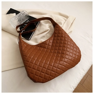 Close-up of brown quilted faux leather tote bag with wide strap on cream fabric