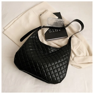 Close-up of black quilted shoulder bag with rhombus patterns and artistic props