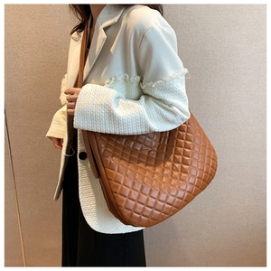 Side view of a large brown quilted tote bag worn with a stylish tweed jacket outfit