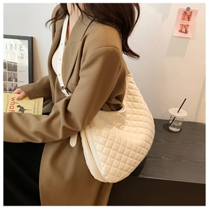 Close-up of white quilted crescent bag with adjustable strap on a shoulder