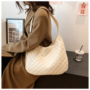 Close-up of a white quilted shoulder bag with wide leather strap in a cafe setting