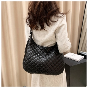 Detail view of a large black quilted tote bag with shiny finish worn by a model